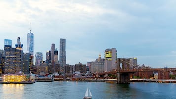 A city skyline with a prominent bridge and a sailboat on the water.