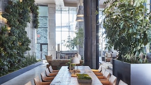Un comedor amplio con una larga mesa de madera rodeada de sillas de cuero, grandes lámparas colgantes y diversas plantas.