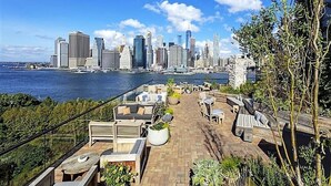 Terraza en la azotea con mobiliario exterior, vista del horizonte urbano y un cuerpo de agua.