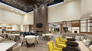 A spacious hotel lobby with multiple seating areas, including yellow armchairs and tables, a large sofa, and a television mounted on a pillar. - Homewood Suites By Hilton Irvine John Wayne Airport (Irvine)