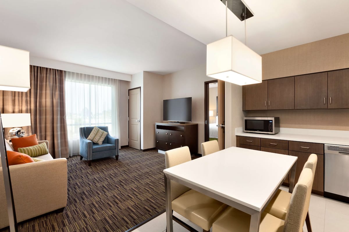 A hotel room with a dining area, a TV, a microwave, and a sofa with pillows.