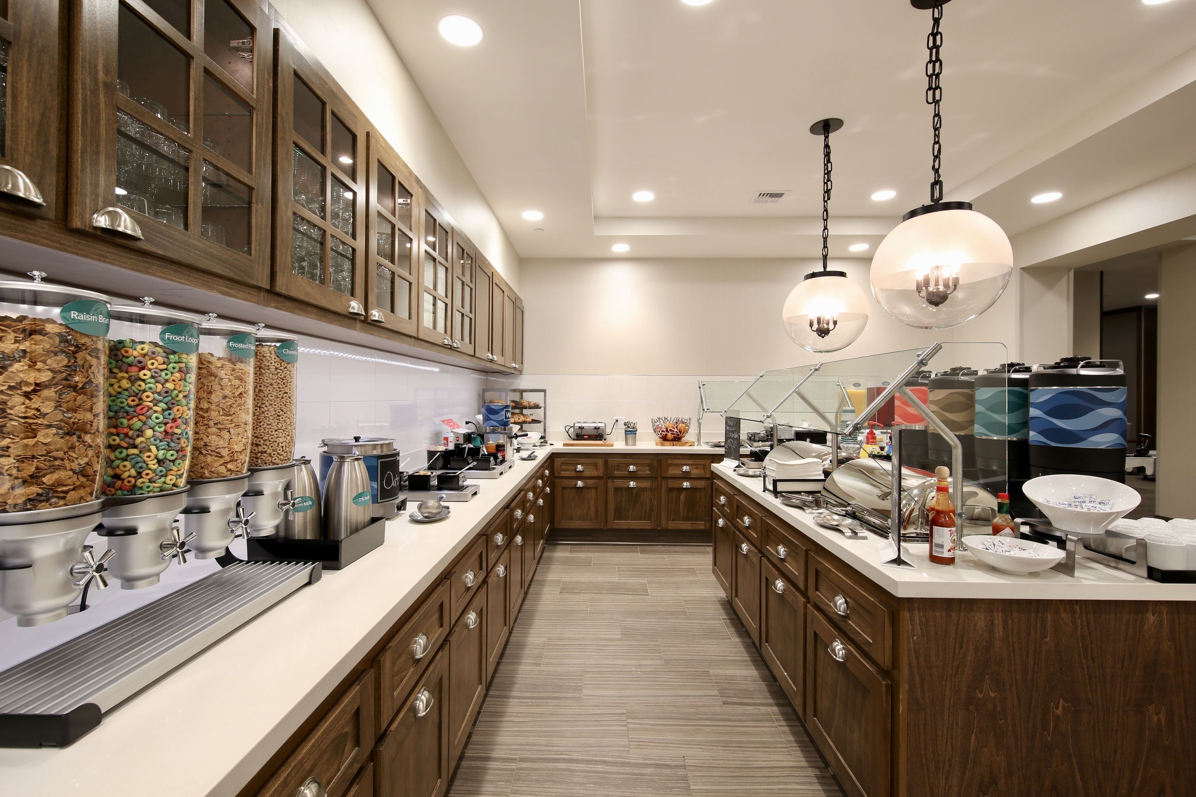 A modern kitchen with a long counter, food dispensers, and wooden cabinets.