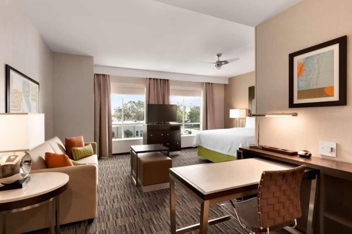 A hotel room with a bed, a desk, a chair, a TV, a dresser, and a window with curtains.