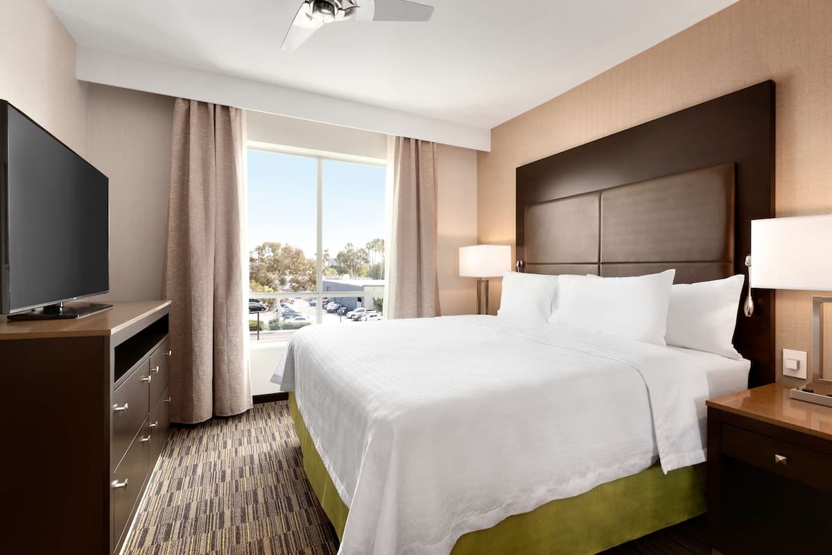 A hotel room with a large bed, a television, a desk, and a window with curtains.