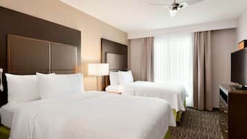 A hotel room with two beds, a desk, a television, and a ceiling fan.