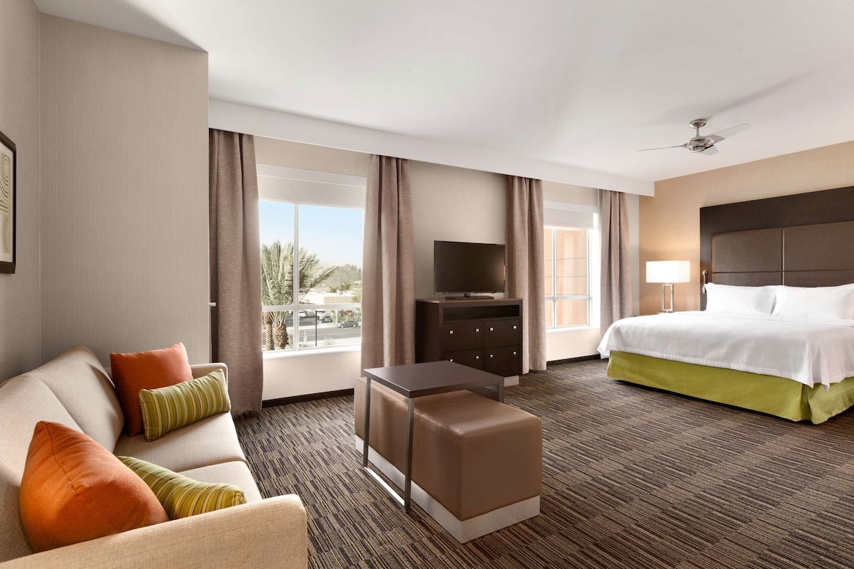 Habitación de hotel con cama, sofá, televisor, escritorio y vista al exterior.