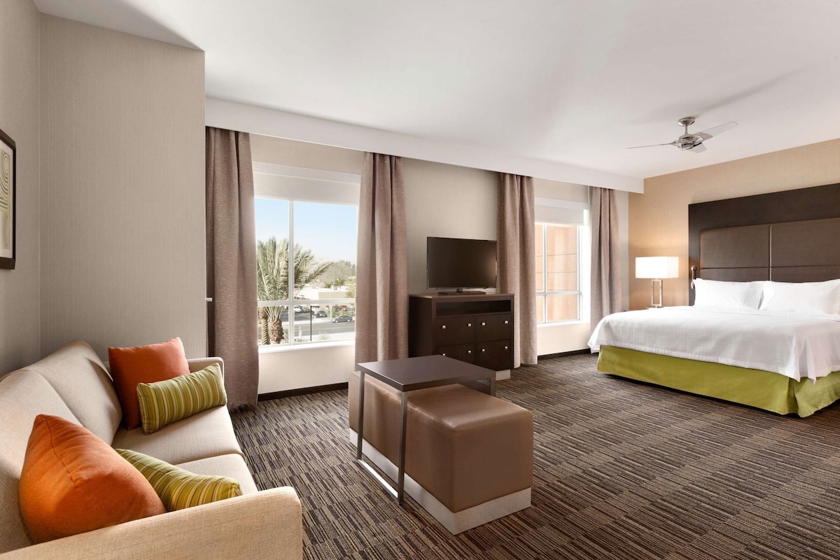 Habitación de hotel con cama, sofá, televisor, escritorio y vista al exterior.