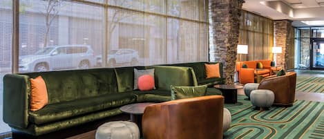 Un hall d’entrée avec un canapé vert, des poufs et des fauteuils orange.