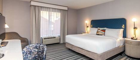A hotel room with a bed, a desk, a chair, and a window with curtains.
