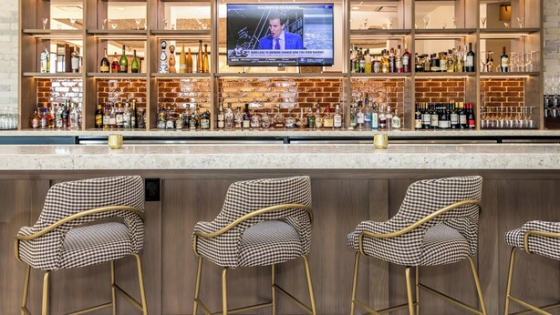 A bar area with a television screen, bar stools, and a variety of bottles and glasses. - voco The Clair Cincinnati Downtown by IHG (Cincinnati)