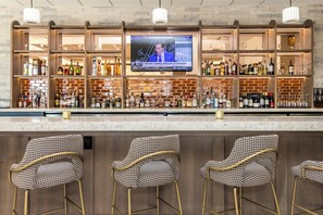 A bar area with a television screen, bar stools, and a variety of bottles and glasses. - voco The Clair Cincinnati Downtown by IHG (Cincinnati)