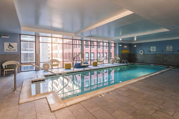 An indoor swimming pool with clear glass walls, a pool lift, and a lifeguard station. - voco The Clair Cincinnati Downtown by IHG (Cincinnati)