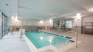 Una piscina interior con una silla de socorrista, sillas junto a la piscina y una vista despejada del área de la piscina.
