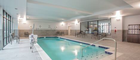 Una piscina interior con una silla de socorrista, sillas junto a la piscina y una vista despejada del área de la piscina.