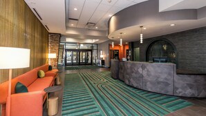 A lobby with a reception desk, a seating area with orange sofas, and a patterned carpet. - voco The Clair Cincinnati Downtown by IHG (Cincinnati)