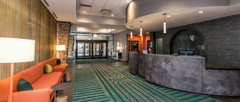 A lobby with a reception desk, a seating area with orange sofas, and a patterned carpet.