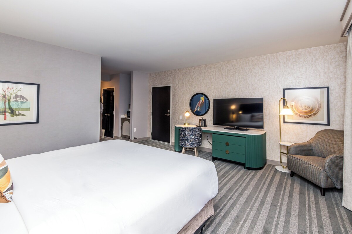 Een hotelkamer met een groot bed, een bureau met een televisie, een stoel en een lamp.