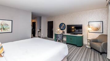 Habitación de hotel con una cama grande, un escritorio con televisor, una silla y una lámpara.