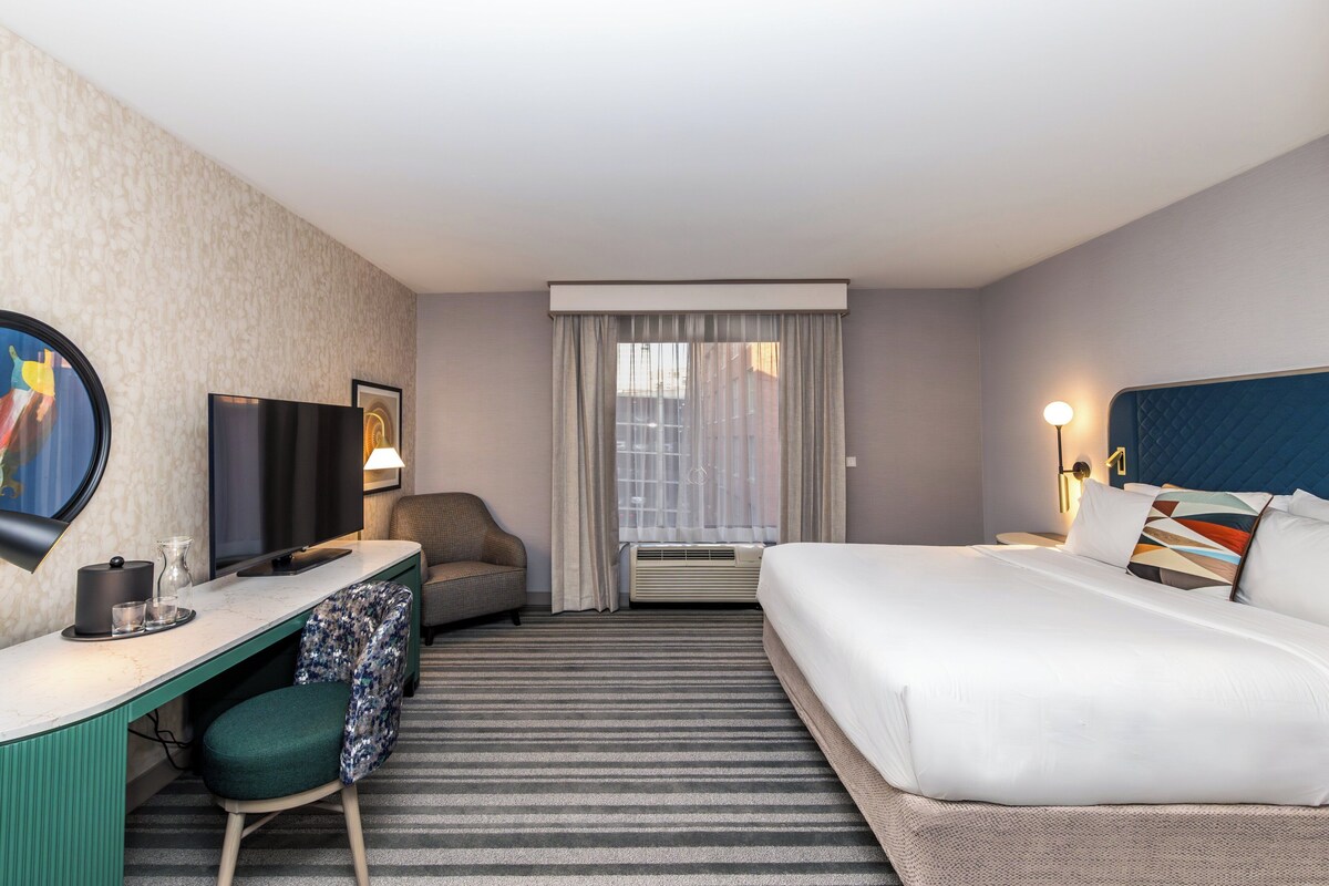 Een hotelkamer met een bed, een bureau met stoel, een televisie en een raam met gordijnen.