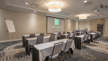 Une salle de conférence équipée de tables et de chaises, un écran de projection affichant un logo et un panneau indiquant la sortie.