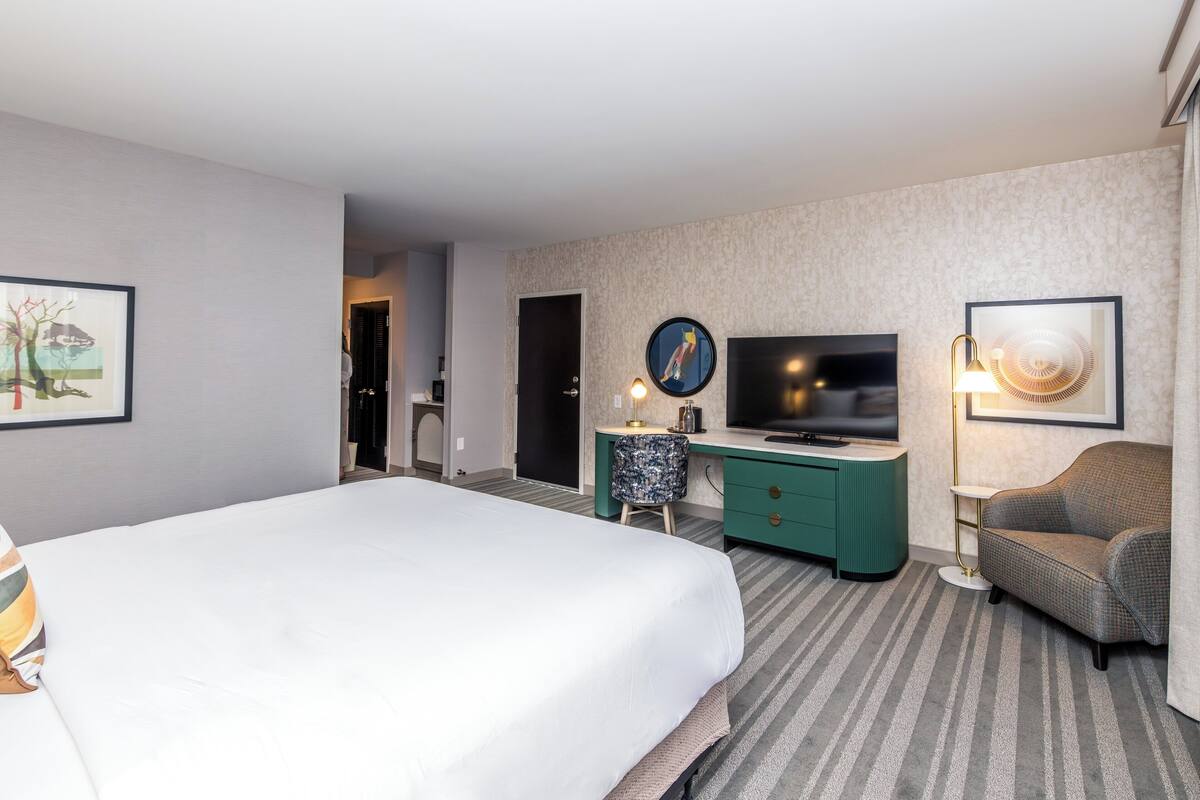Une chambre d’hôtel avec un grand lit, un bureau avec une télévision, une chaise et une lampe.