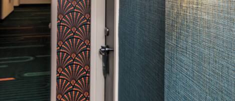 A hallway with a patterned wall, a door, and a wall-mounted light fixture.