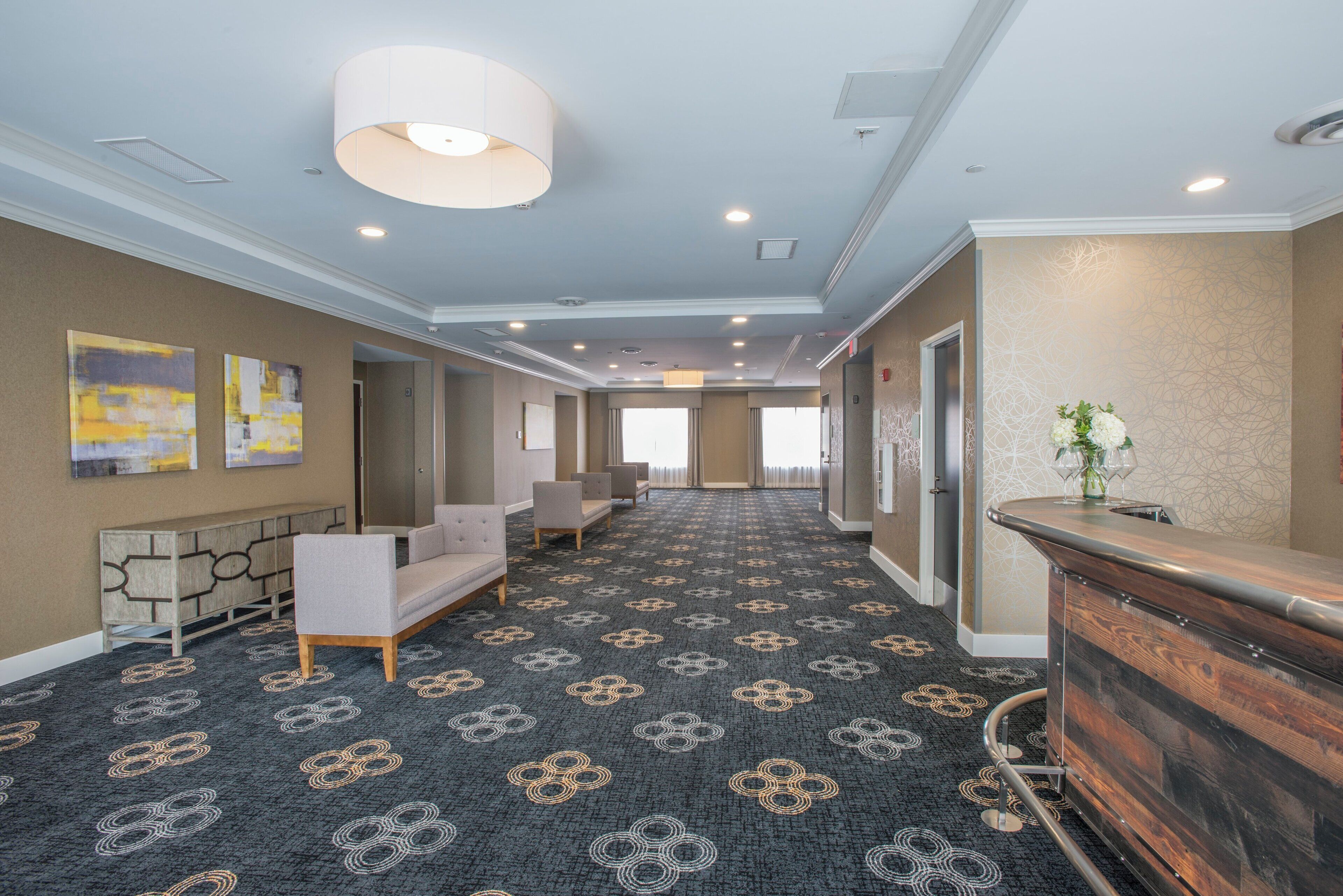 A hotel lobby with a patterned carpet, seating area, reception desk, and artwork on the walls.