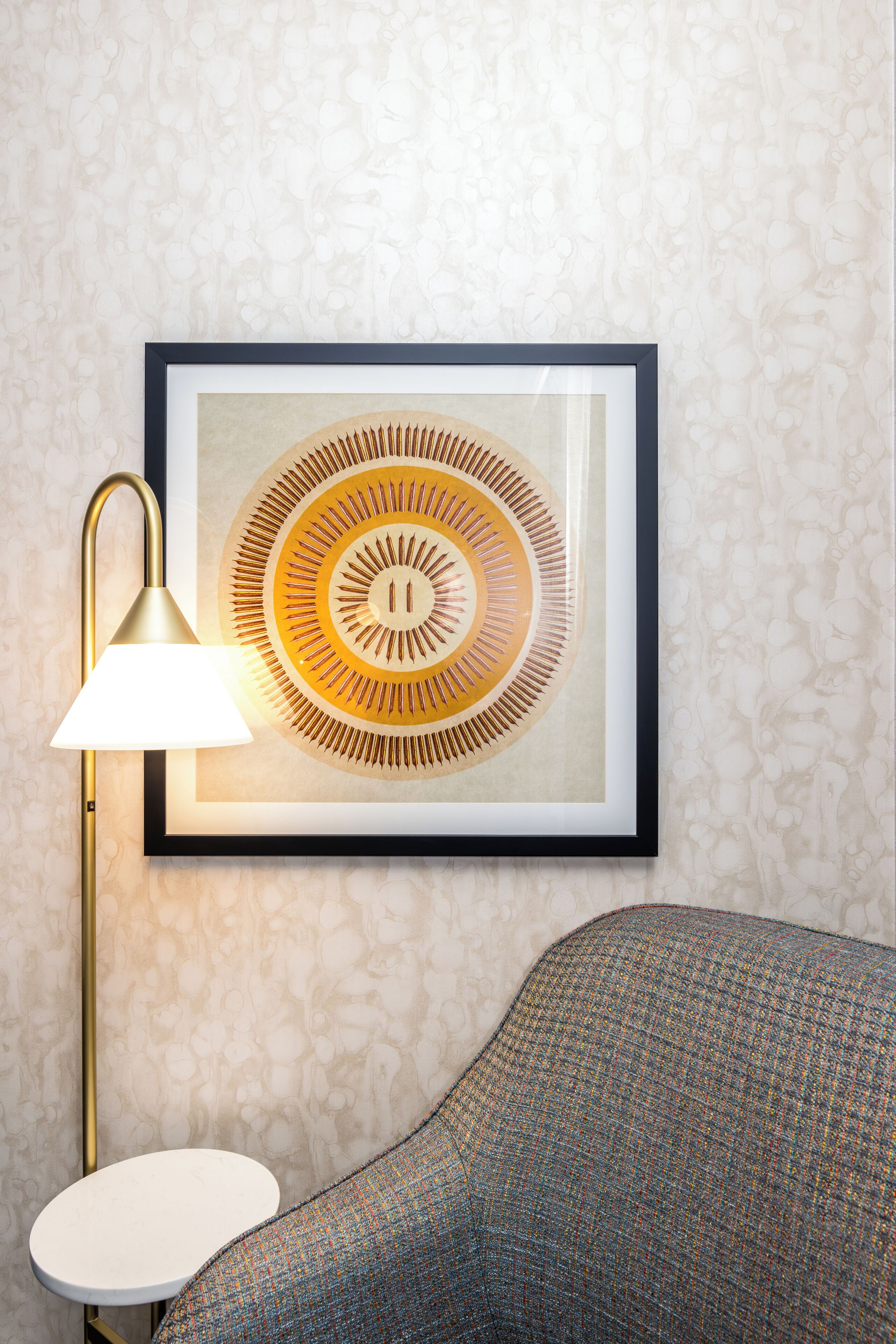 Una obra de arte abstracta enmarco con un diseño circular, una lámpara de pie moderna y un sofá con textura.