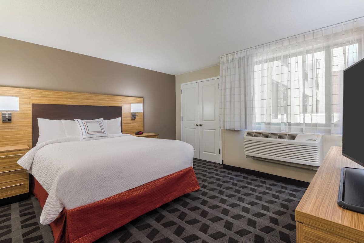 A hotel room with a bed, a desk, a TV, a wardrobe, and an air conditioning unit.