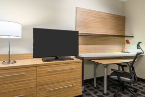 Une chambre d’hôtel moderne dotée d’un bureau en bois, d’un téléviseur à écran plat, d’une lampe, d’une chaise et d’une étagère intégrée.