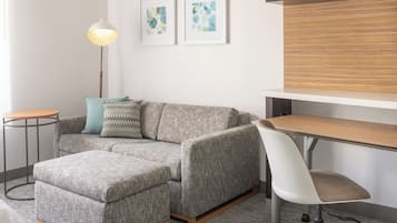 Una sala de estar moderna con un sofá gris, una mesita redonda pequeña, una lámpara de pie y un escritorio de madera.