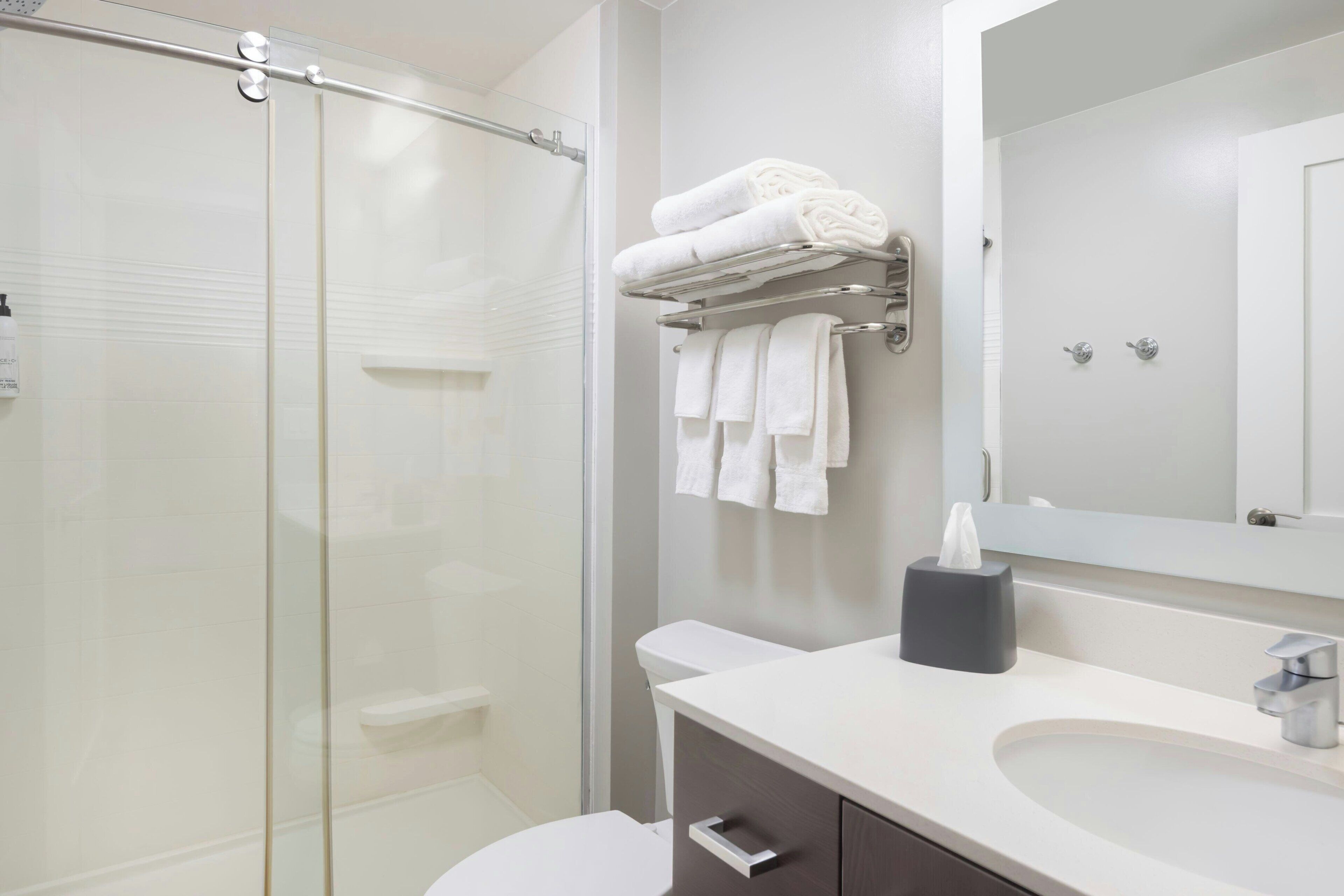 Un baño moderno con cabina de ducha de vidrio, inodoro blanco, tocador con espejo y toallero con toallas dobladas.