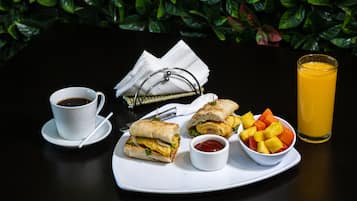 Un vassoio con due panini, una tazza di caffè, un bicchiere di succo d'arancia e una ciotola di frutta.