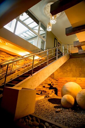 A staircase with a metal railing leading to a higher level, a skylight above, and large spherical objects on the lower level. - Terra Bella Hotel Boutique (San Salvador)