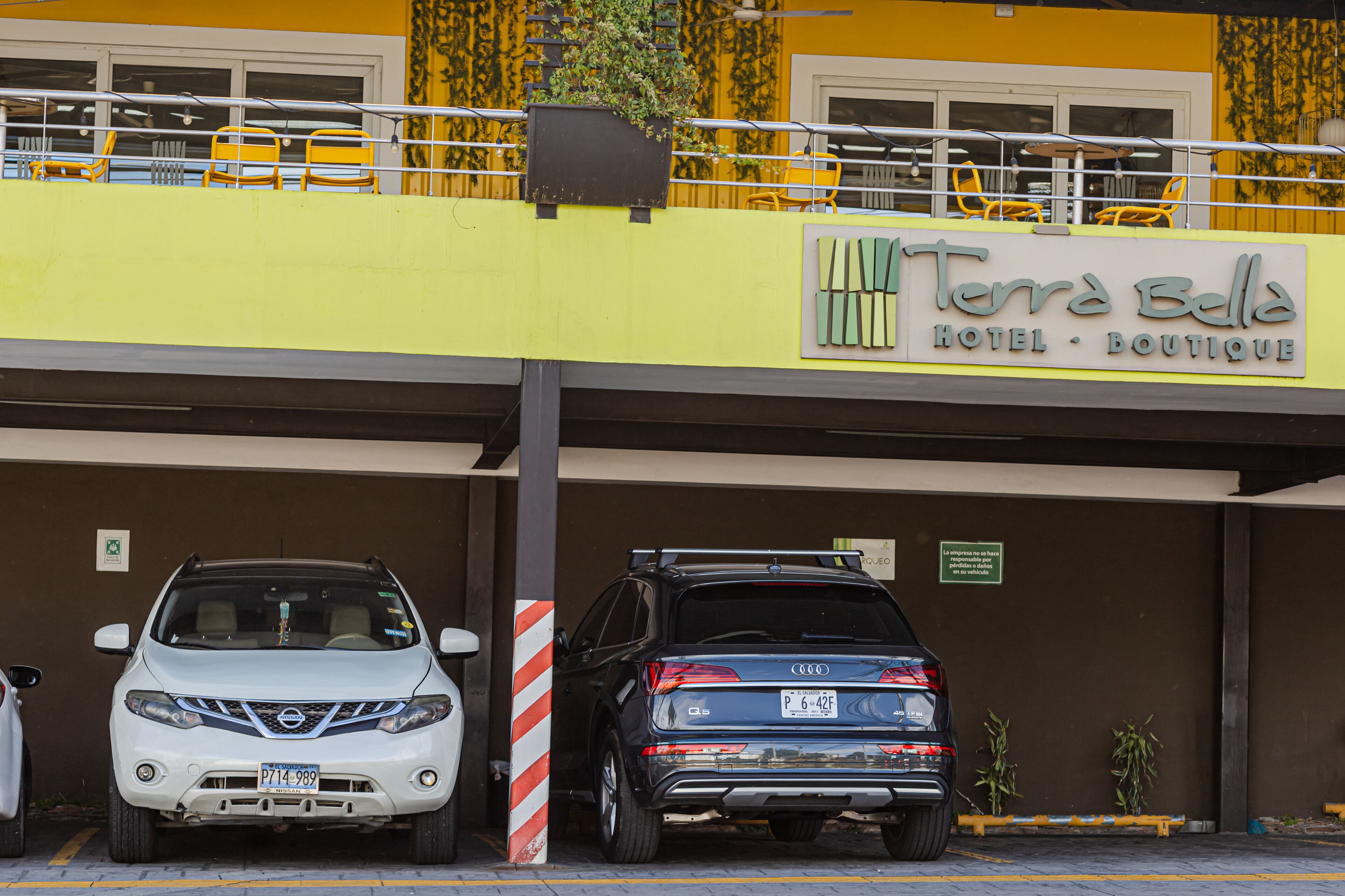 Un estacionamiento con dos coches, un edificio amarillo con un cartel que dice 