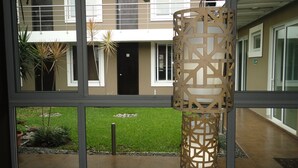 A modern building with large windows, a courtyard with grass and plants, and a hanging wooden light fixture. - Terra Bella Hotel Boutique (San Salvador)