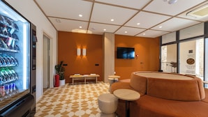 Un hall d’hôtel équipé d’un distributeur automatique, d’un espace salon et d’un téléviseur à écran plat fixé au mur.