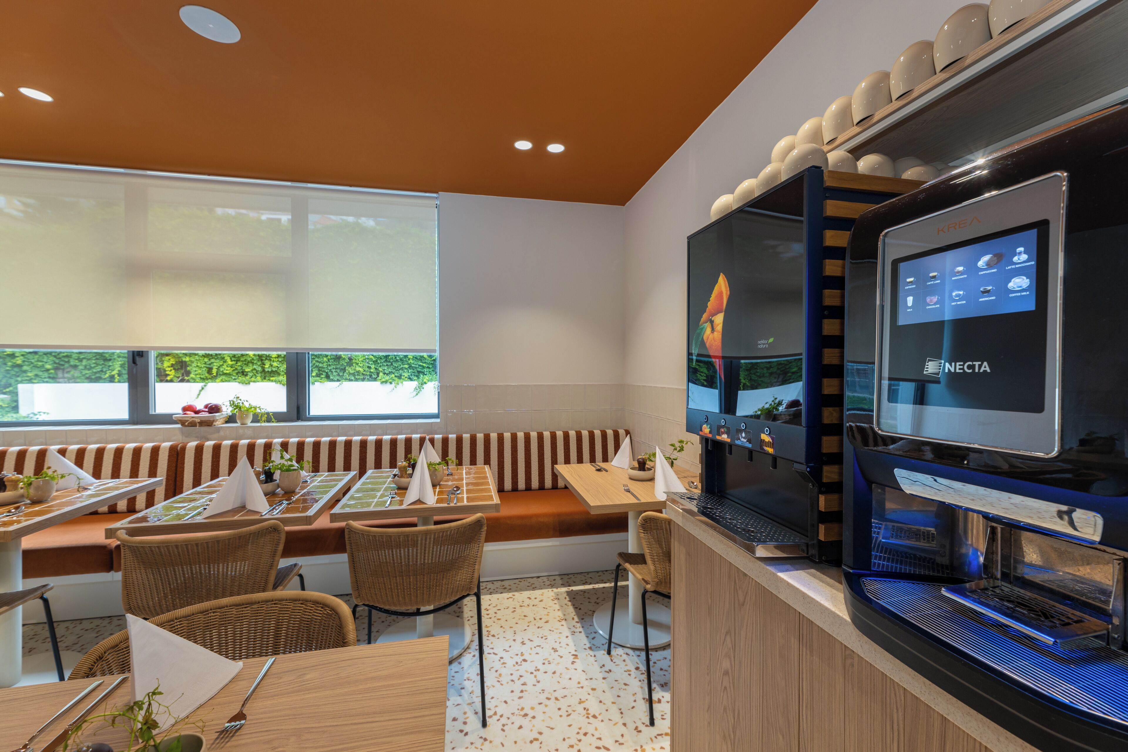 A modern restaurant with a seating area, a coffee machine, and a window with a view.