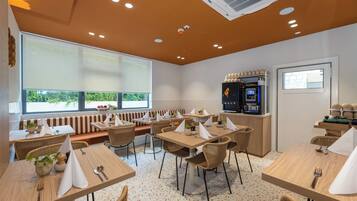A modern dining area with wooden tables, wicker chairs, and a view of greenery outside.