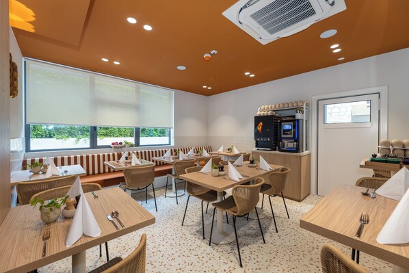 A modern dining area with wooden tables, wicker chairs, and a view of greenery outside. - B&B Sol (Dubrovnik)