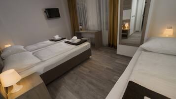 A hotel room with a large bed, a smaller bed, a desk with a chair, a TV mounted on the wall, and a mirror reflecting the room.