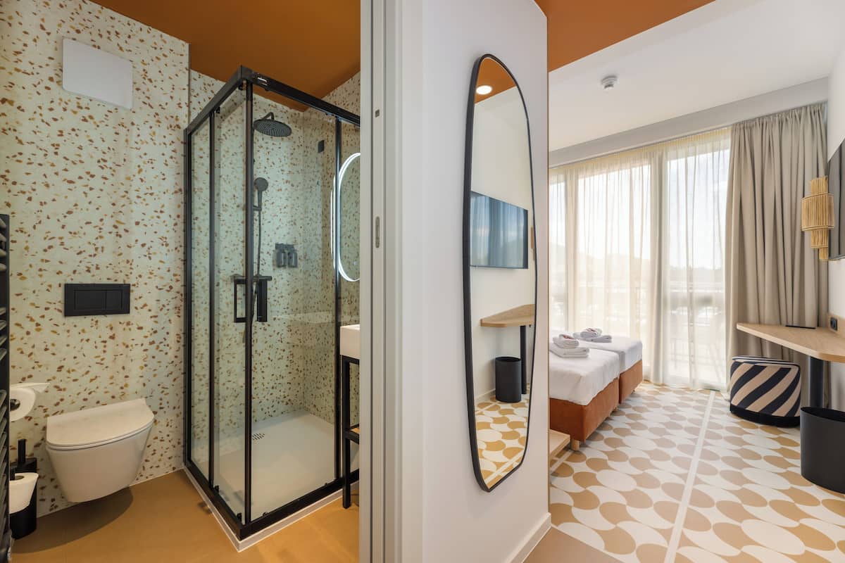 A hotel room with a shower, toilet, bed, and a large mirror.