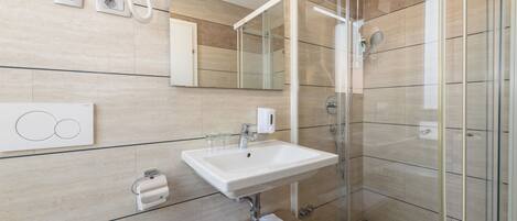 Un baño moderno con cabina de ducha de vidrio, un lavamanos blanco y un espejo encima.