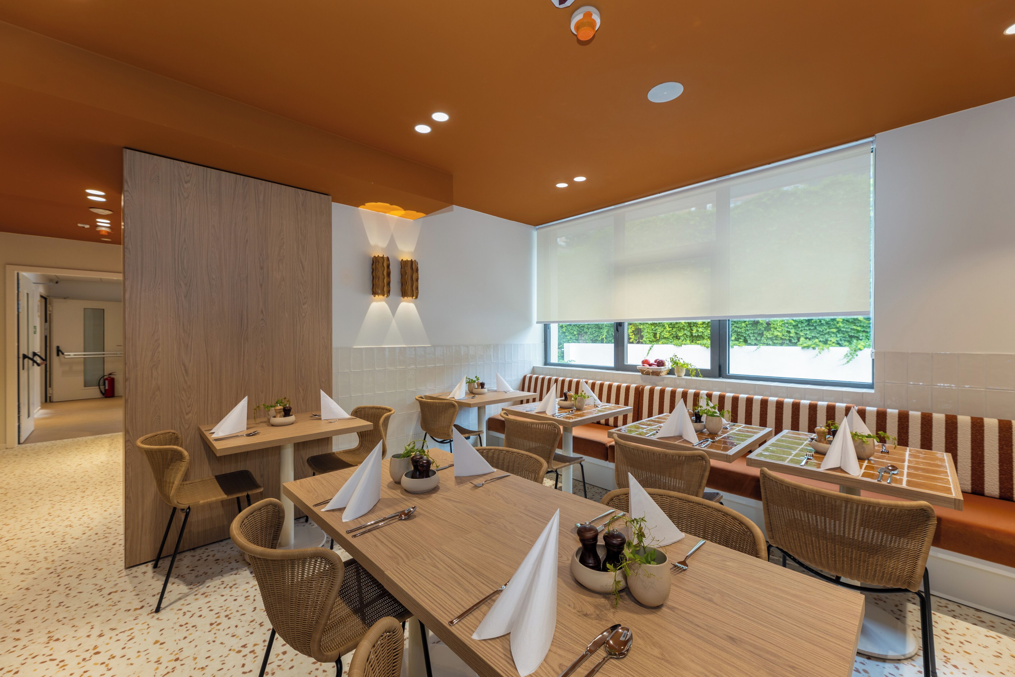 A modern dining area with wooden tables, wicker chairs, and a large window with a view.