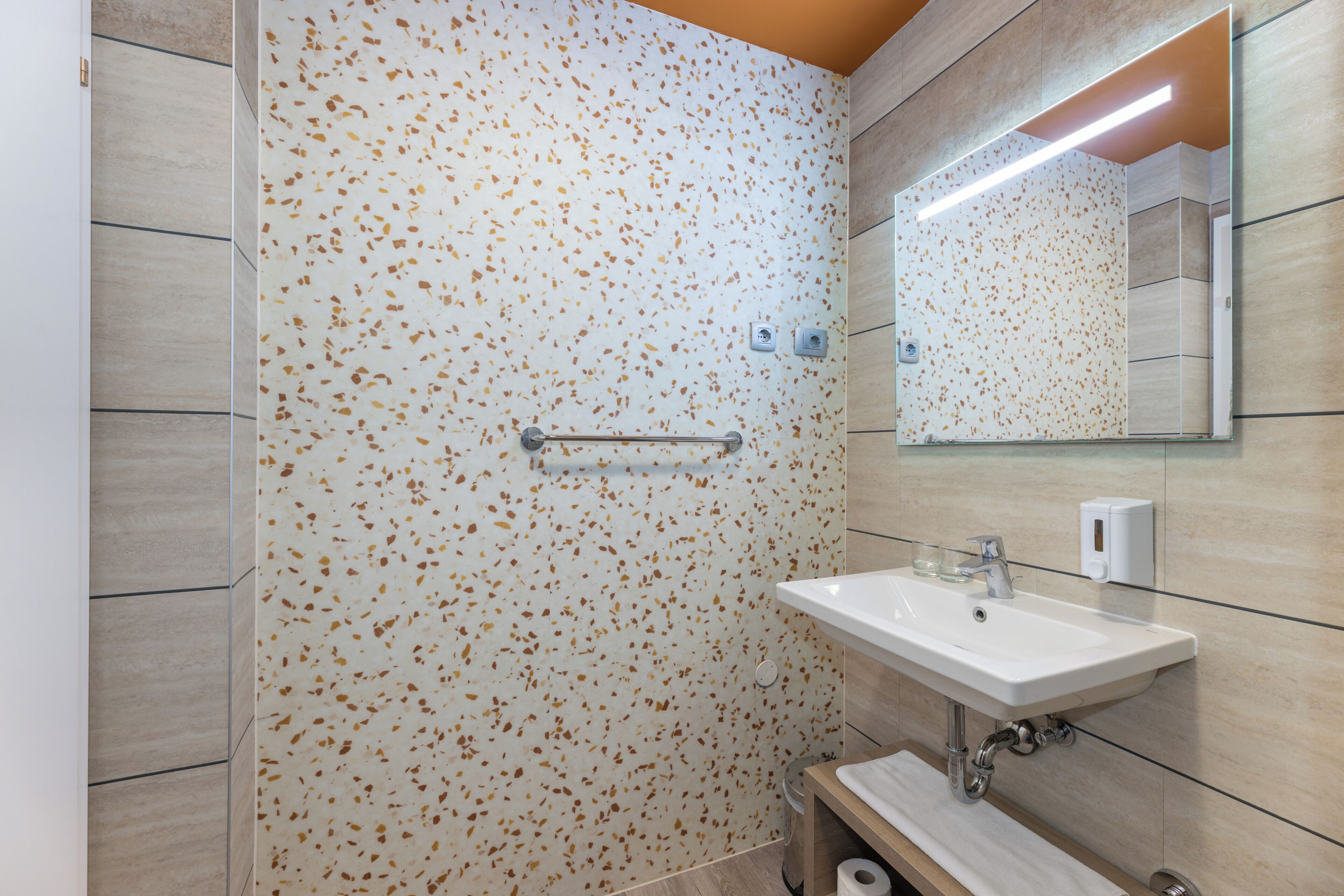 Un baño con pared de baldosas veteadas, un lavamanos con espejo y un perchero.