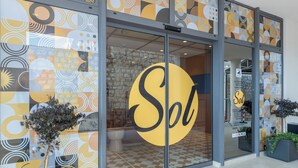Un bâtiment avec une grande enseigne jaune sur la porte vitrée, portant l’inscription « Sol », un intérieur avec des murs en pierre et un sol carrelé.