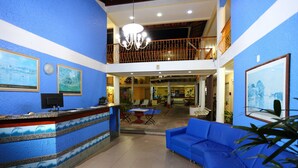 A hotel lobby with a reception desk, blue walls, a chandelier, a blue sofa, and a balcony with a railing. - Marlim Porto Hotel (Porto Seguro)