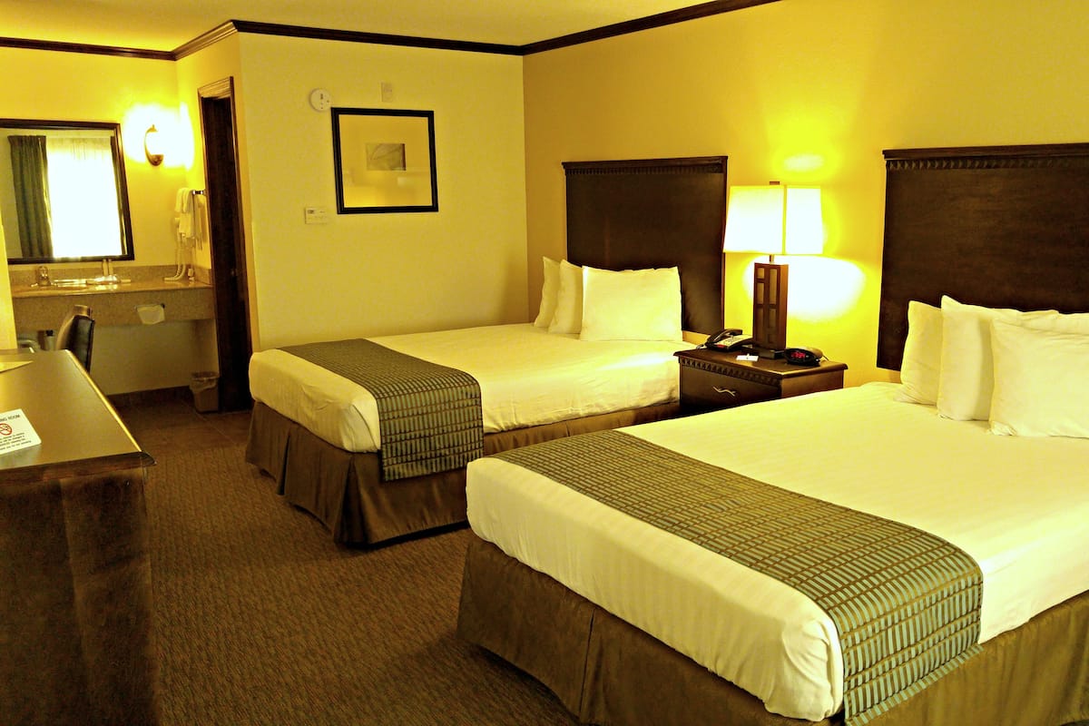 A hotel room with two beds, a desk, a mirror, and a nightstand with a lamp.