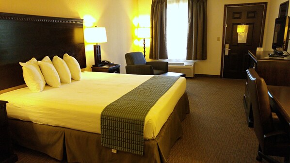 Una habitación de hotel con una cama grande, dos lámparas de noche, una silla, un escritorio con una computadora y una puerta con un cartel.