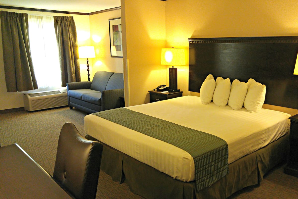 A hotel room with a large bed, two bedside tables with lamps, a chair, a desk, and a wall-mounted air conditioner.
